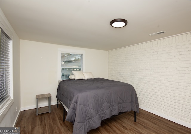 bedroom with dark wood-type flooring and brick wall