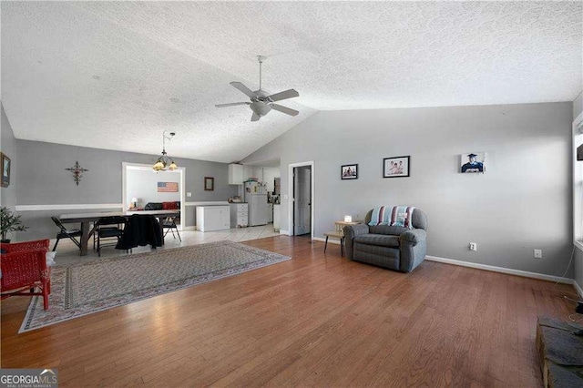 living room featuring ceiling fan with notable chandelier, hardwood / wood-style floors, a textured ceiling, and vaulted ceiling