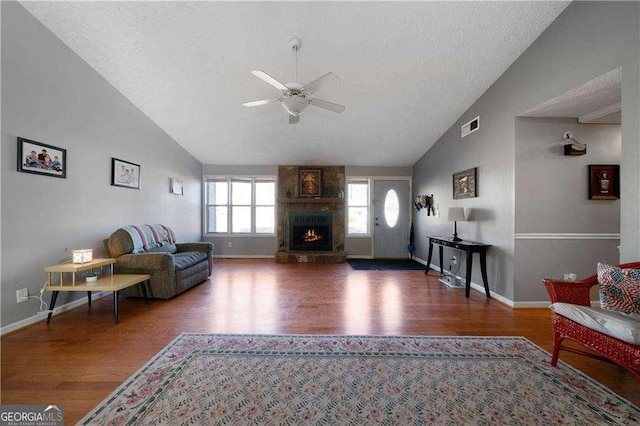 living room with lofted ceiling, hardwood / wood-style flooring, ceiling fan, a fireplace, and a textured ceiling