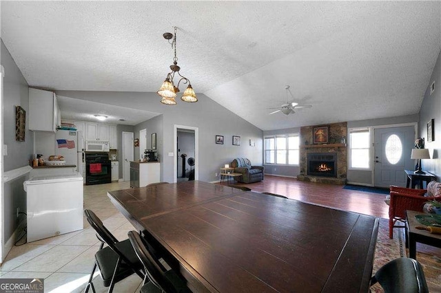 tiled dining area featuring a textured ceiling, a fireplace, ceiling fan with notable chandelier, and lofted ceiling