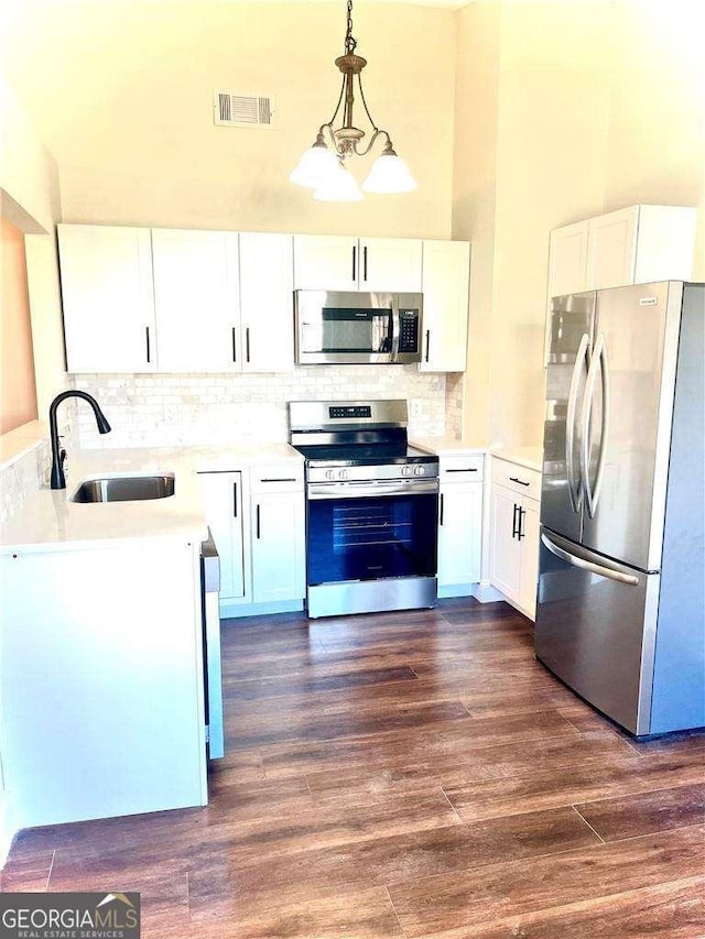 kitchen featuring stainless steel appliances, dark wood-type flooring, pendant lighting, a chandelier, and white cabinetry