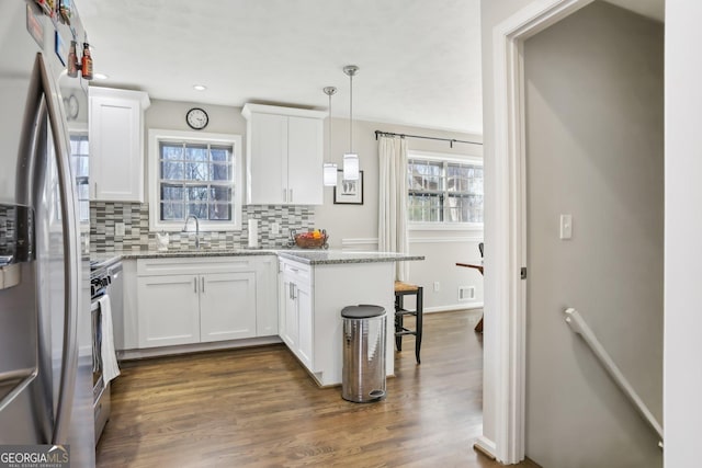 kitchen with white cabinets, stainless steel fridge, kitchen peninsula, and pendant lighting