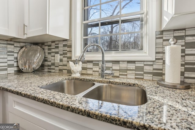 details with tasteful backsplash, white cabinetry, sink, and light stone counters