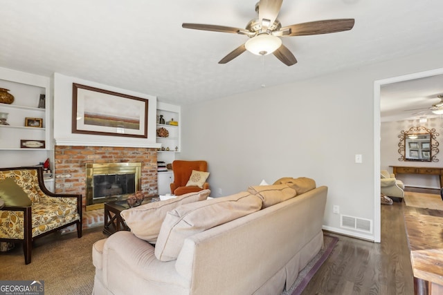 living room with a fireplace, built in features, ceiling fan, and dark wood-type flooring