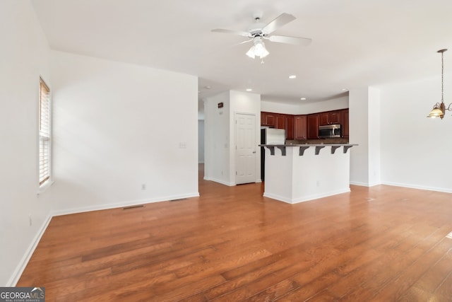 unfurnished living room featuring ceiling fan with notable chandelier and hardwood / wood-style flooring