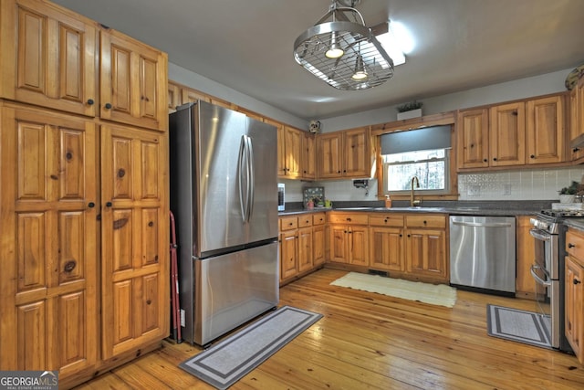 kitchen with tasteful backsplash, sink, light hardwood / wood-style floors, and appliances with stainless steel finishes