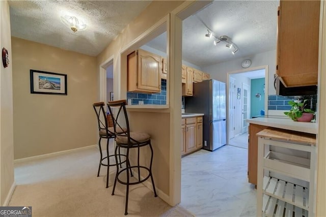 kitchen featuring rail lighting, stainless steel fridge, a textured ceiling, decorative backsplash, and a breakfast bar