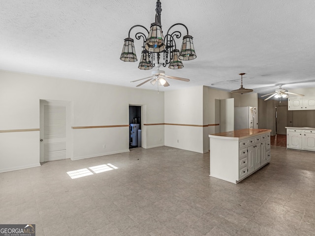 kitchen featuring pendant lighting, white refrigerator, a textured ceiling, a kitchen island, and ceiling fan with notable chandelier