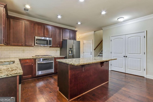 kitchen with a center island, backsplash, light stone countertops, ornamental molding, and appliances with stainless steel finishes