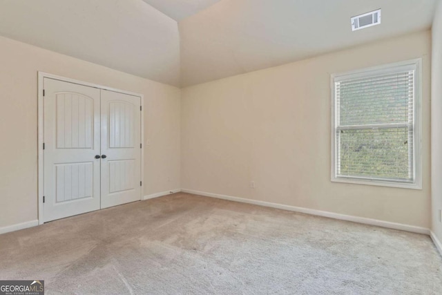 unfurnished bedroom with light colored carpet, lofted ceiling, and a closet