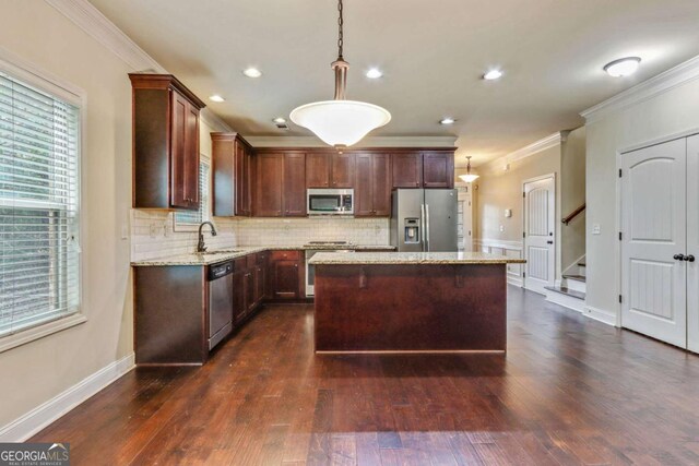 kitchen featuring sink, hanging light fixtures, light stone countertops, a kitchen island, and stainless steel appliances