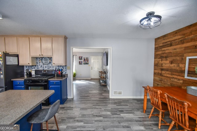 kitchen with blue cabinets, wooden walls, black gas stove, stainless steel refrigerator, and light brown cabinetry