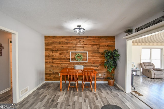 dining area featuring a textured ceiling, wood walls, and hardwood / wood-style flooring