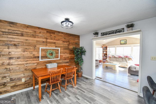 dining room featuring a textured ceiling, wooden walls, and hardwood / wood-style floors