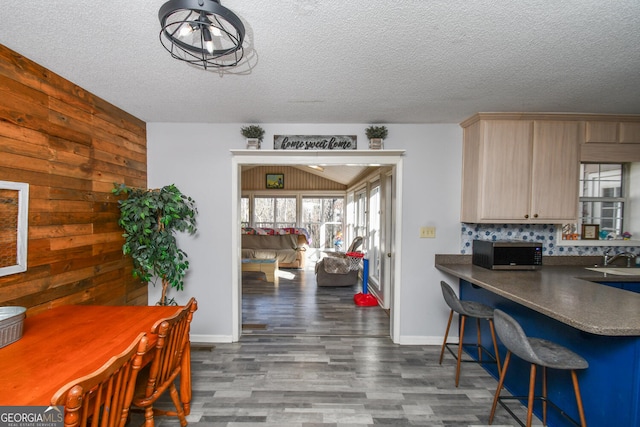 kitchen with light brown cabinets, wood walls, backsplash, and a textured ceiling