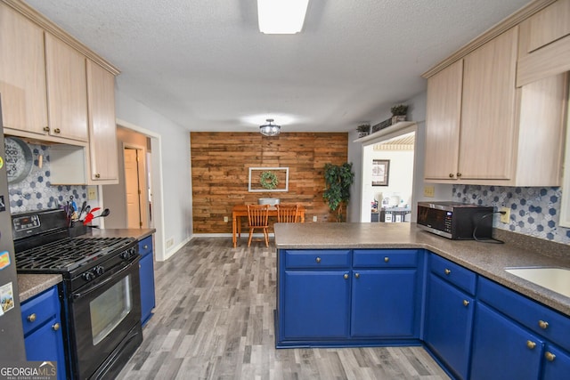 kitchen featuring black gas range, wood walls, kitchen peninsula, light brown cabinets, and blue cabinets