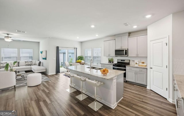 kitchen with appliances with stainless steel finishes, dark hardwood / wood-style flooring, a kitchen breakfast bar, sink, and a center island with sink