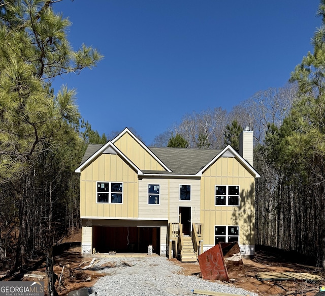 view of front of property featuring board and batten siding, driveway, a chimney, and a garage