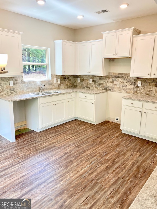 kitchen with visible vents, white cabinets, a sink, light wood-type flooring, and backsplash