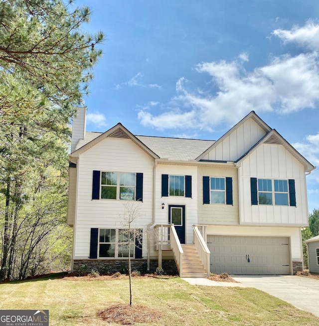 split foyer home featuring board and batten siding, a front yard, stone siding, and driveway