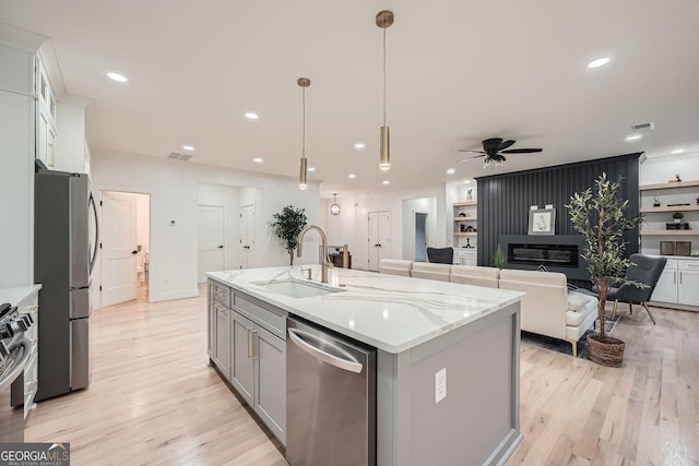 kitchen with pendant lighting, sink, stainless steel appliances, white cabinets, and a center island with sink