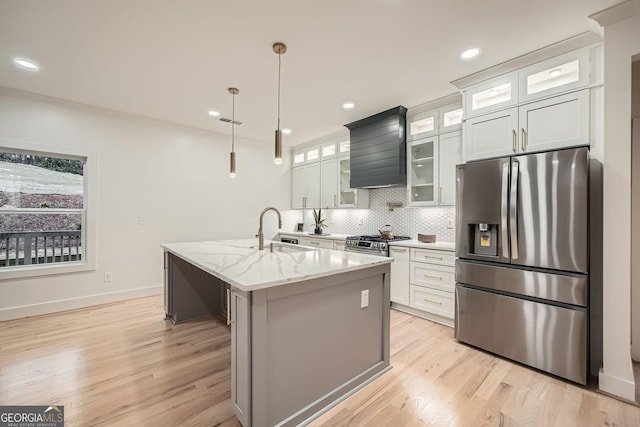 kitchen featuring appliances with stainless steel finishes, sink, white cabinets, a kitchen island with sink, and light stone counters