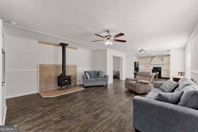 living room featuring ceiling fan, ornamental molding, a wood stove, and dark hardwood / wood-style floors