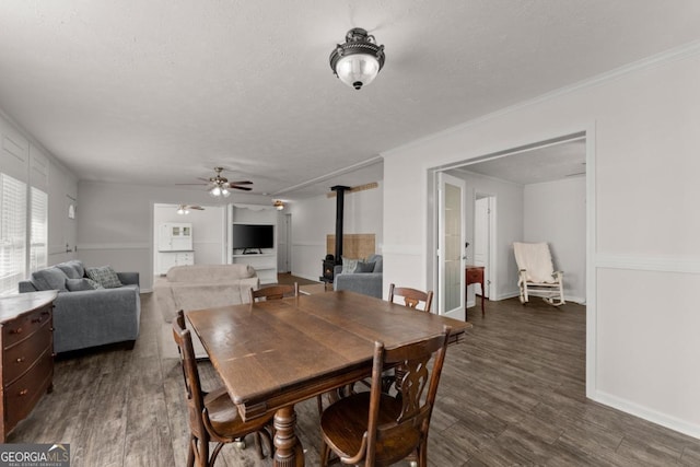 dining area featuring dark wood-type flooring, a textured ceiling, ceiling fan, and a wood stove