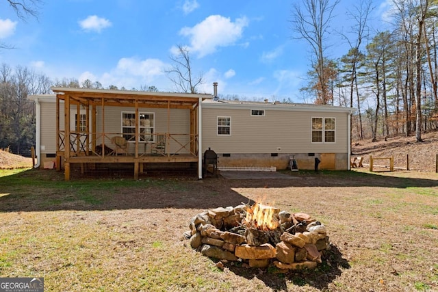 rear view of house featuring a deck, a lawn, and a fire pit