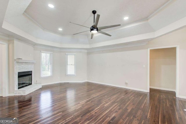 unfurnished living room with dark wood-type flooring, a raised ceiling, ceiling fan, and ornamental molding