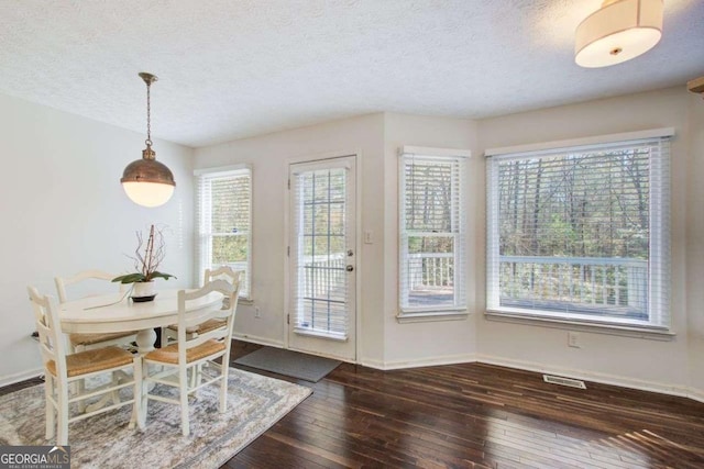 dining area with a textured ceiling, a healthy amount of sunlight, and dark hardwood / wood-style floors