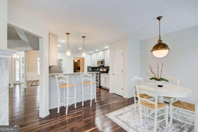 kitchen featuring kitchen peninsula, appliances with stainless steel finishes, decorative backsplash, and white cabinetry