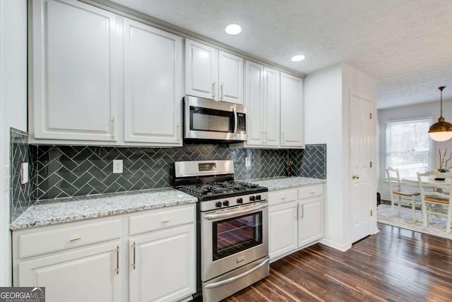 kitchen with a textured ceiling, stainless steel appliances, decorative light fixtures, white cabinets, and dark hardwood / wood-style floors