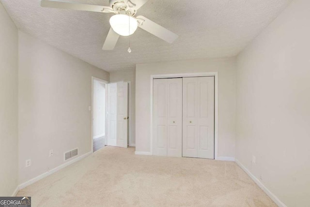 unfurnished bedroom with a textured ceiling, carpet floors, a closet, and ceiling fan