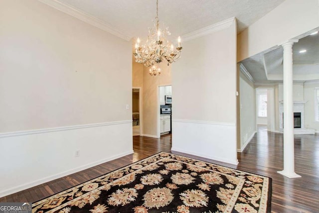 spare room featuring dark wood-type flooring, a notable chandelier, decorative columns, crown molding, and a textured ceiling