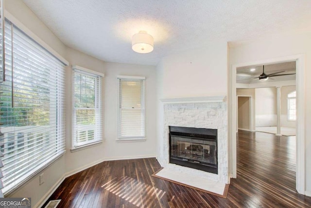 unfurnished living room featuring a stone fireplace, ceiling fan, dark wood-type flooring, and a textured ceiling