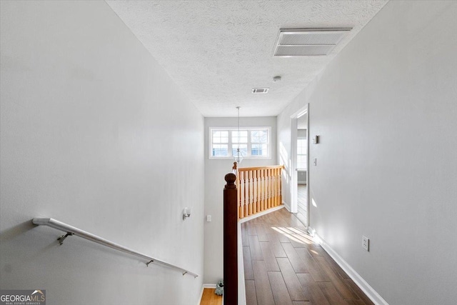 hallway featuring a textured ceiling, visible vents, dark wood-style flooring, and an upstairs landing