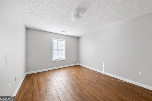 empty room with a textured ceiling, baseboards, and wood finished floors