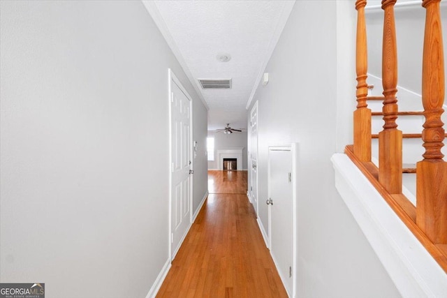 hallway with light wood-style floors, baseboards, visible vents, and a textured ceiling