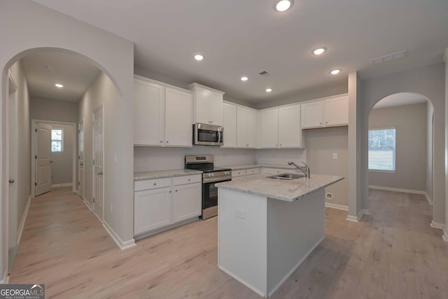 kitchen with white cabinetry, sink, a kitchen island with sink, stainless steel appliances, and light stone countertops