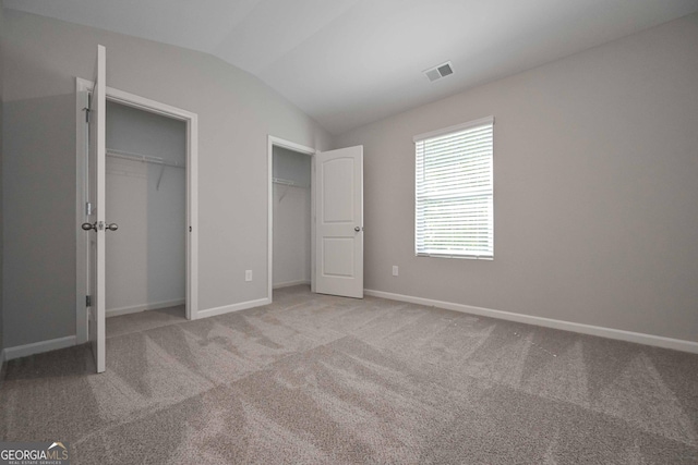 unfurnished bedroom featuring light colored carpet, vaulted ceiling, and two closets