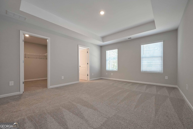 unfurnished bedroom featuring a closet, a walk in closet, light colored carpet, and a raised ceiling