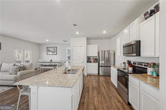 kitchen with dark hardwood / wood-style floors, stainless steel appliances, an island with sink, white cabinetry, and sink