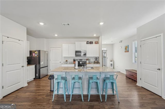 kitchen with a breakfast bar area, a center island with sink, appliances with stainless steel finishes, light stone countertops, and white cabinets