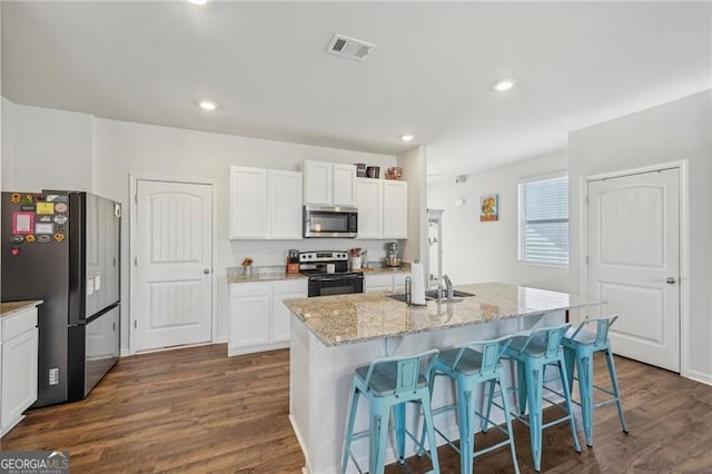 kitchen with white cabinets, stainless steel appliances, a kitchen island with sink, and light stone counters