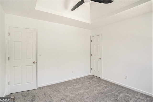 spare room with a raised ceiling, light carpet, ceiling fan, and a textured ceiling