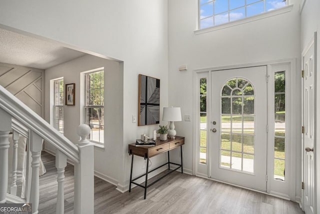 foyer entrance featuring a textured ceiling, a high ceiling, and light hardwood / wood-style flooring