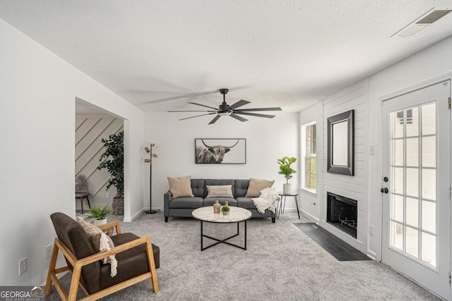 carpeted living room featuring a textured ceiling, a large fireplace, and ceiling fan