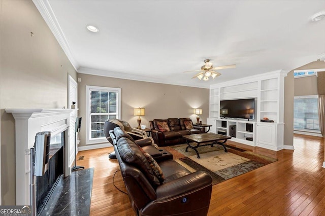 living room featuring ceiling fan, ornamental molding, a high end fireplace, and wood-type flooring