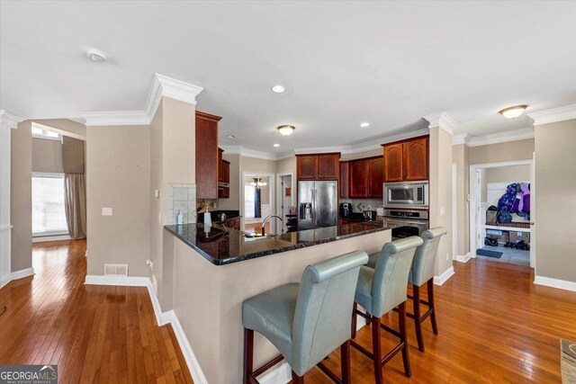 kitchen featuring hardwood / wood-style flooring, appliances with stainless steel finishes, ornamental molding, a kitchen bar, and kitchen peninsula